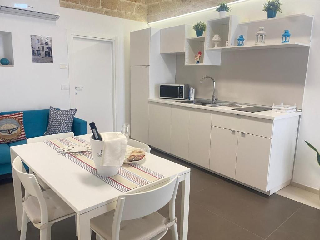 Cocina compacta con armarios blancos, un microondas y un lavamanos. Hay una mesa de comedor con sillas y una botella de vino.