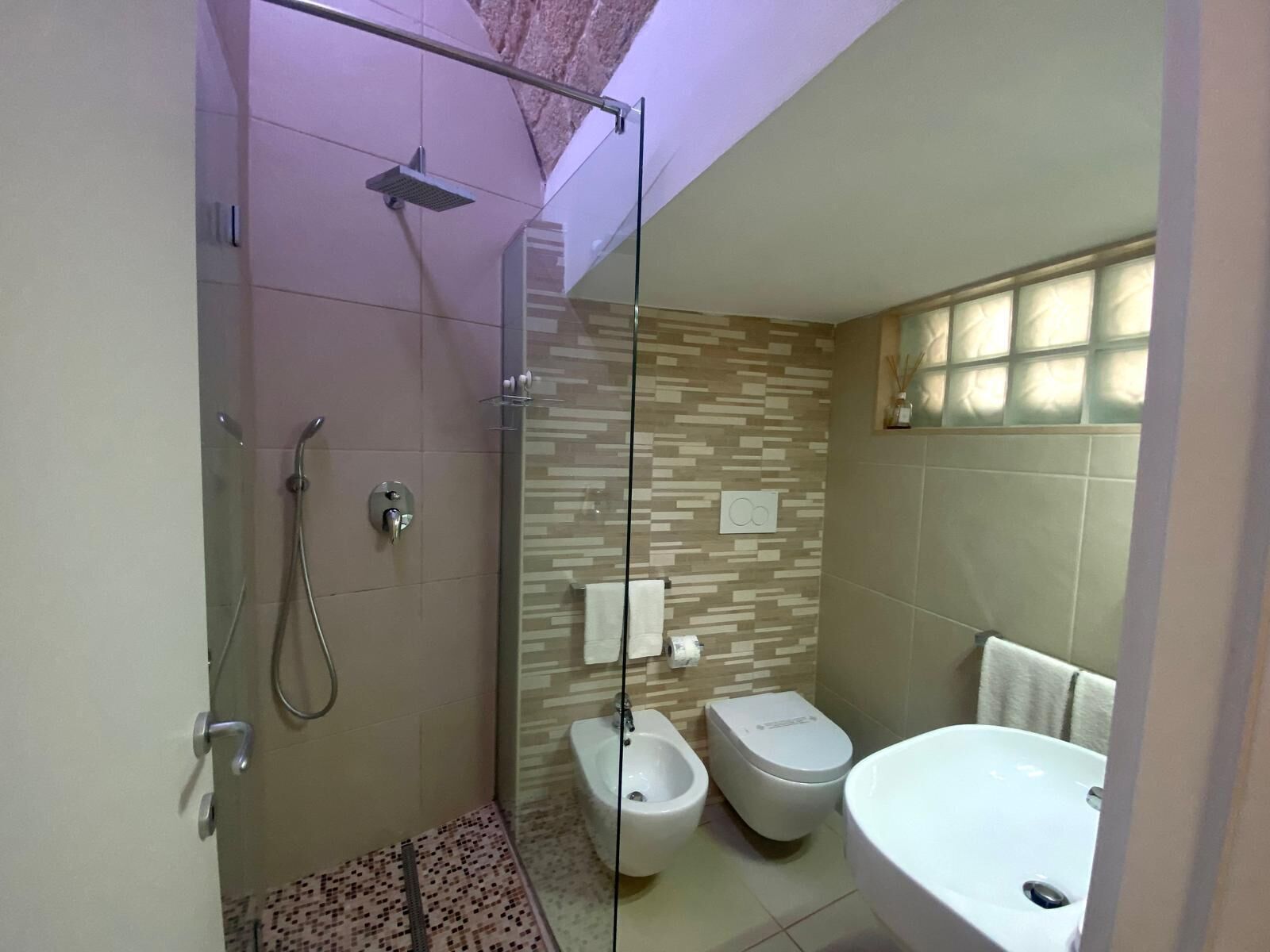 A modern bathroom with a glass-enclosed shower, a bidet, a toilet, and a sink.