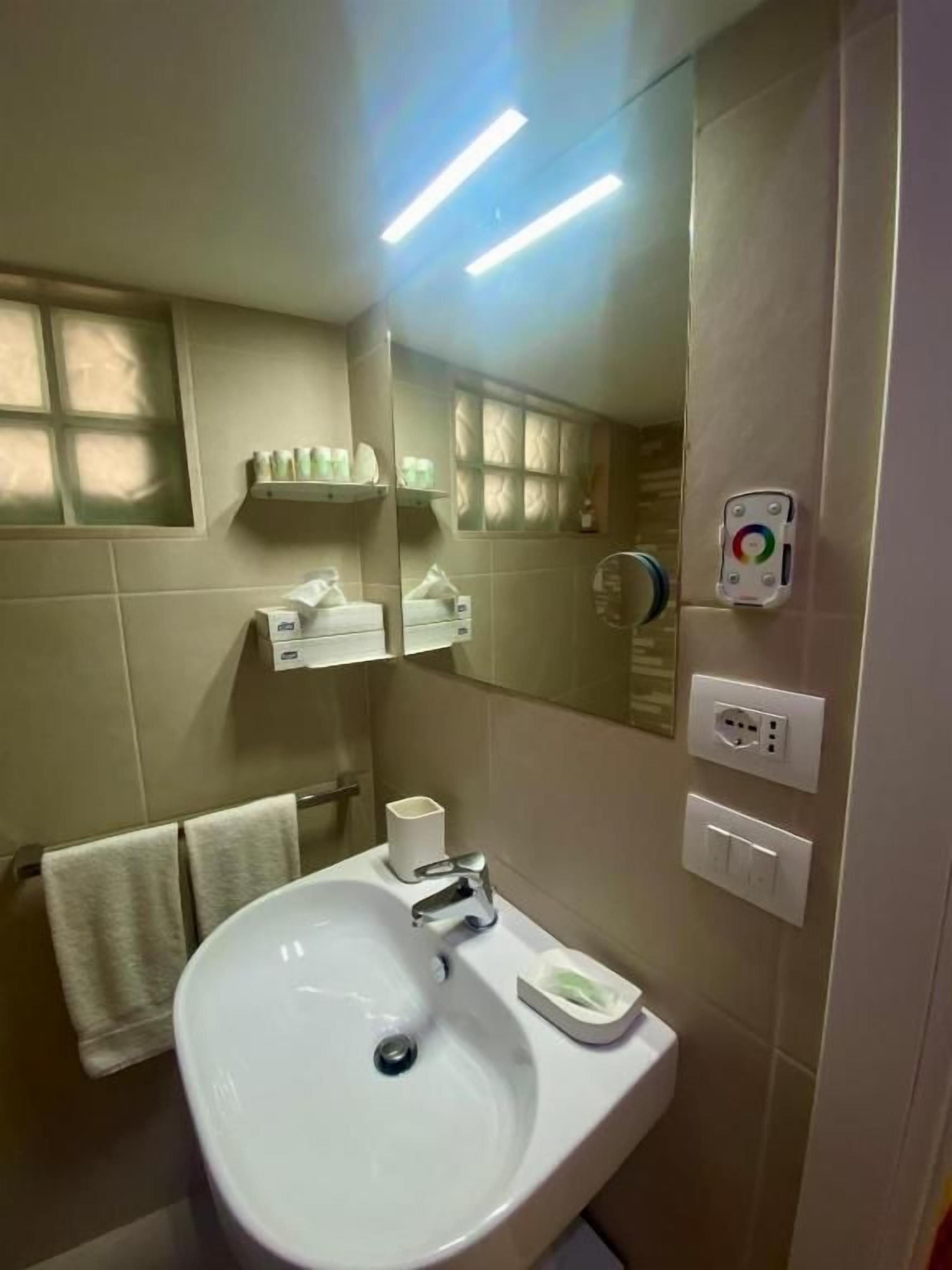 Un baño con lavamanos, espejo, perchero y un enchufe en la pared.