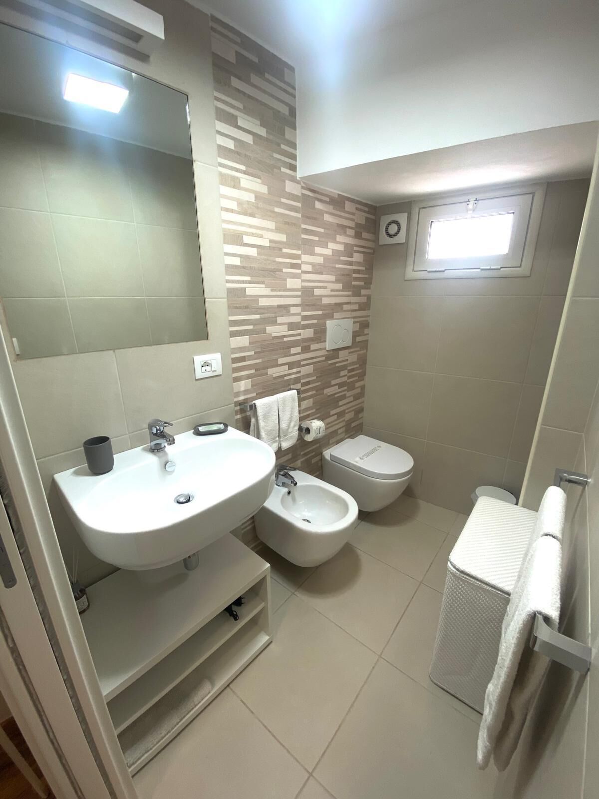 A modern bathroom with a large sink, bidet, toilet, and a small window.