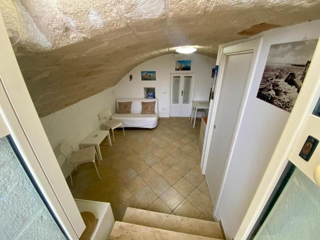 A narrow stairway leading to a room with a white sofa, a small table, and a tiled floor.