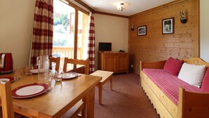 A cozy room with a wooden bed, a dining table set with plates and glasses, and a television on a wooden cabinet.