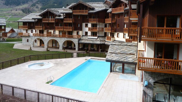 A multi-story hotel with stone arches, wooden balconies, and a swimming pool.