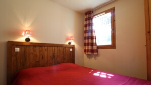 A bedroom with a wooden headboard, two bedside lamps, a plaid curtain, and a window.