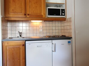 Een keuken met houten kastjes, een magnetron, een vaatwasser en een fornuis.