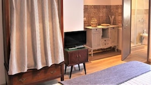 A bedroom with a bed, a TV, a wooden cabinet, a small table, and a bathroom with a shower. - B&B Torre Castellina (Piazza Armerina)