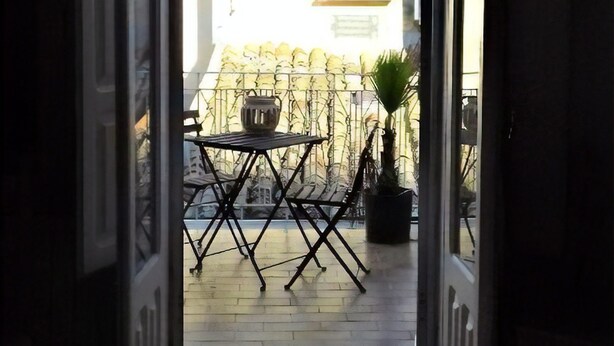 An open doorway leading to an outdoor patio area with a table and chairs, a potted plant, and a view of a building with a tiled roof. - B&B Torre Castellina (Piazza Armerina)