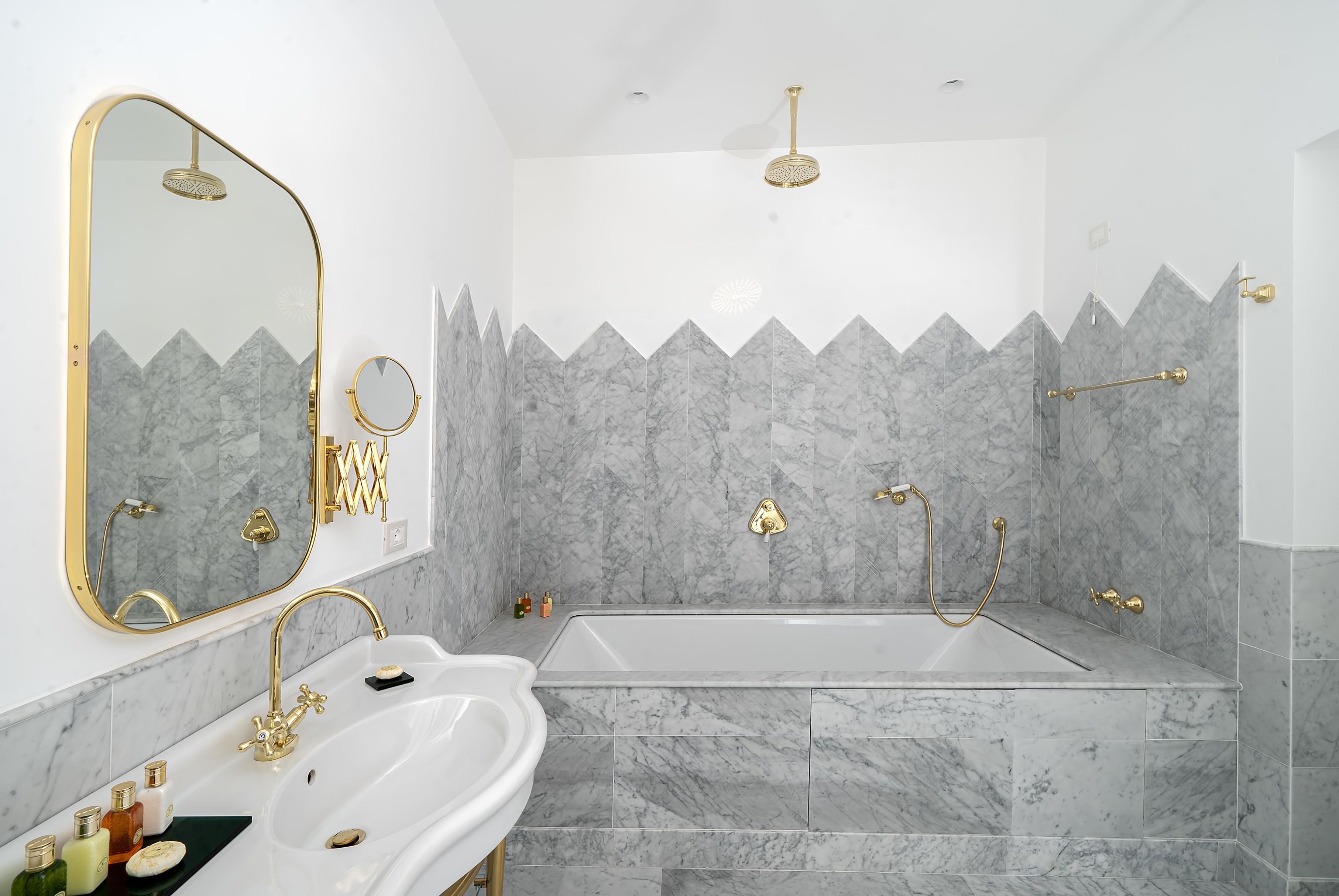 Une salle de bain avec un lavabo blanc, des robinetteries dorées et des murs en marbre.