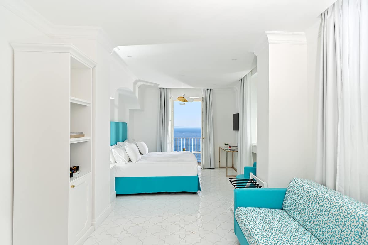 Une chambre d’hôtel avec un lit, un canapé, une télévision et vue sur la mer.