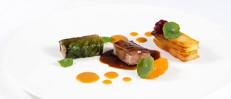 Un plato blanco con diversos alimentos, incluyendo un trozo de carne, verdura y una guarnición de fruta.