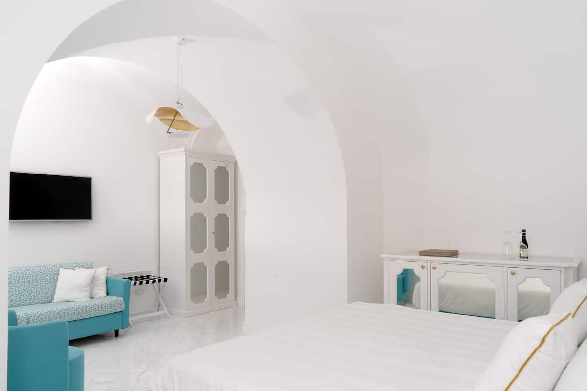 Une chambre moderne avec un lit blanc, un canapé bleu, une armoire blanche et un téléviseur à écran plat fixé au mur.