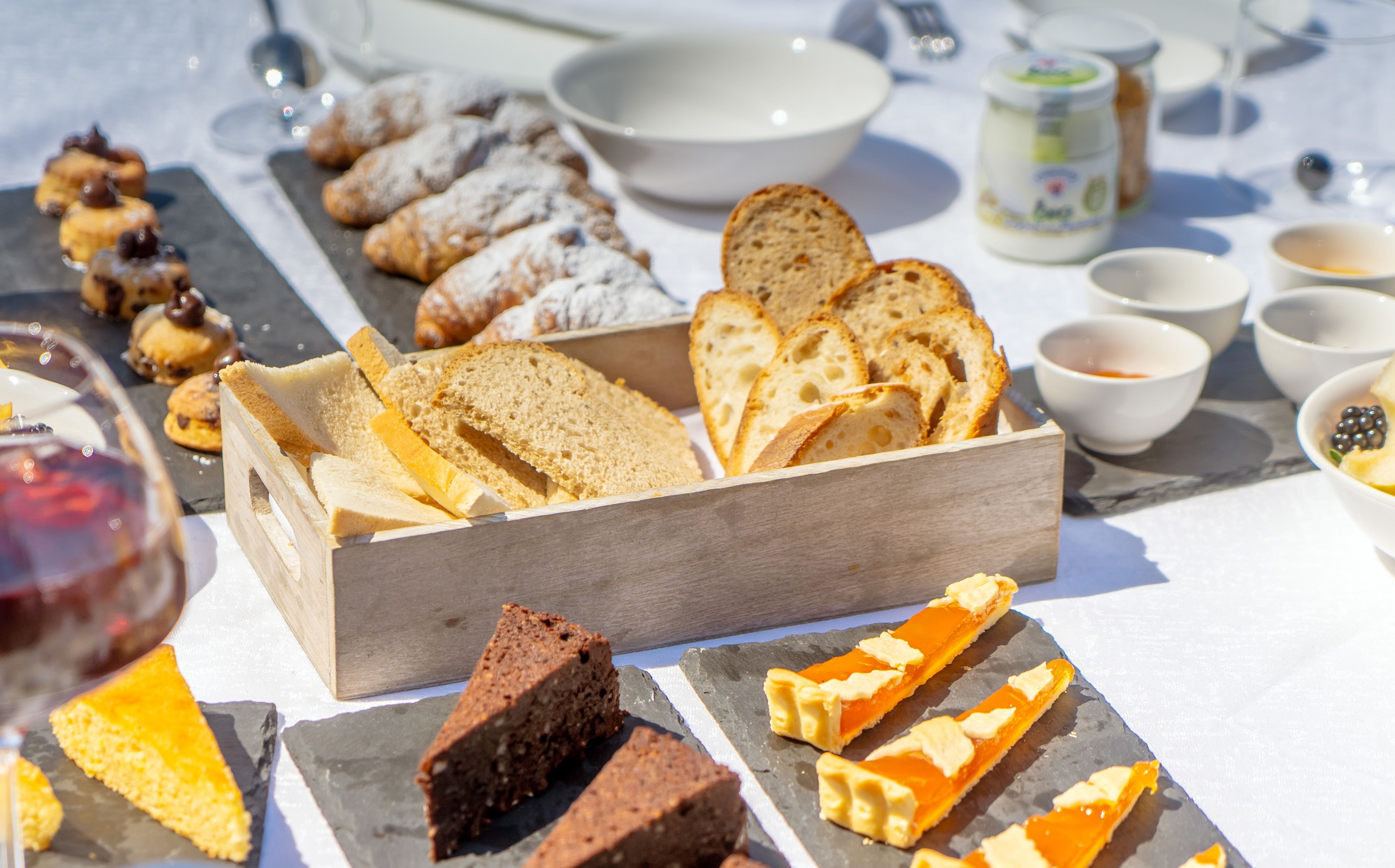 A variety of breads and pastries on a table, including sliced bread, croissants, and a cake.