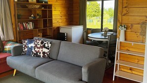 A cozy cabin interior with a gray sofa, wooden shelves, a small table, and a window offering a view of greenery.