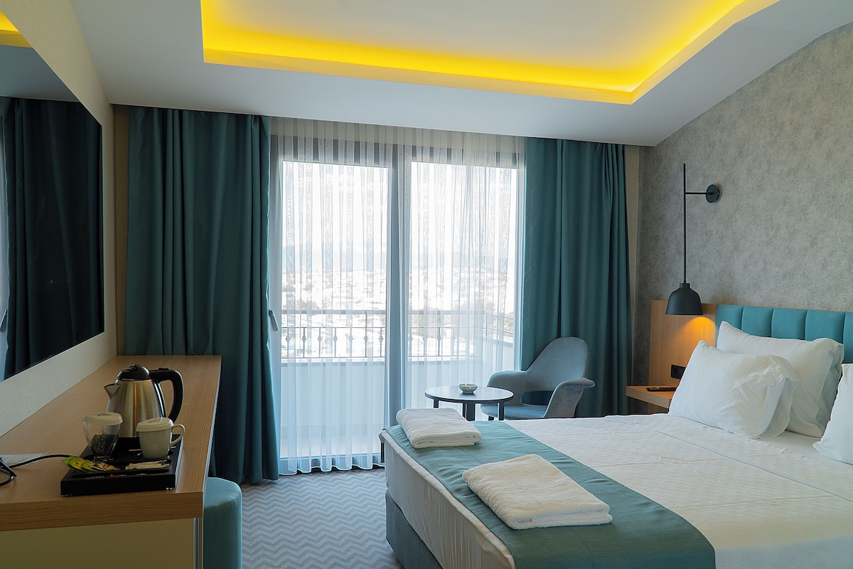 A hotel room with a bed, a desk, a chair, a table, and a lamp.