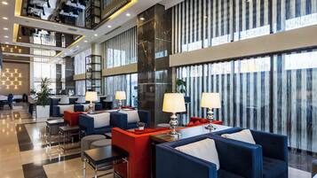 A modern hotel lobby with seating areas, a reception desk, and large windows.