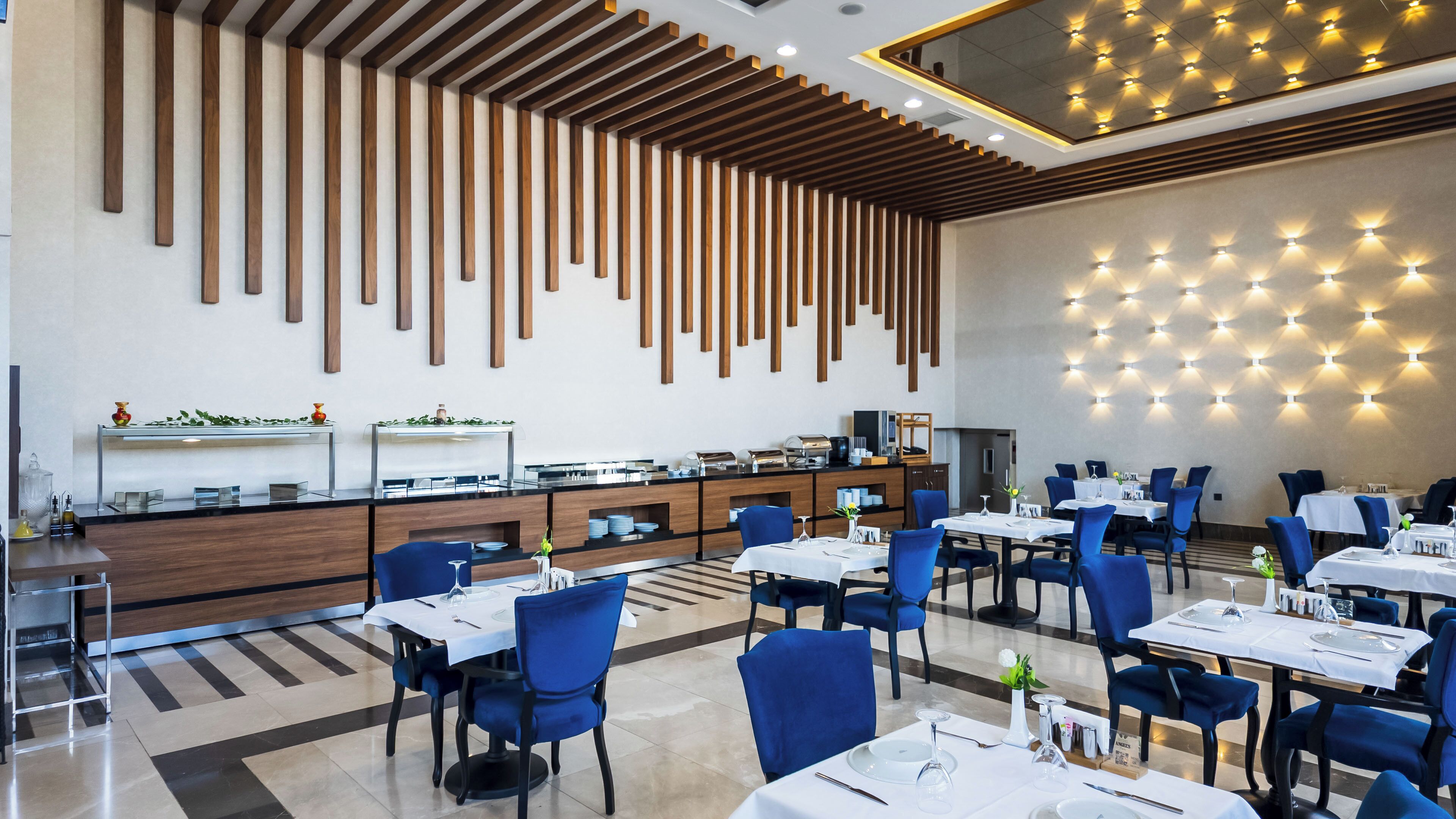 A modern restaurant with a long counter, blue chairs, and a patterned ceiling.