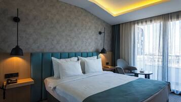 Habitación de hotel moderna con una cama grande, un escritorio, una silla y vistas a la ciudad a través de amplios ventanales.