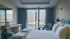Quarto de hotel com cama, escrivaninha, cadeira, mesa pequena e vista da cidade através de grandes janelas.