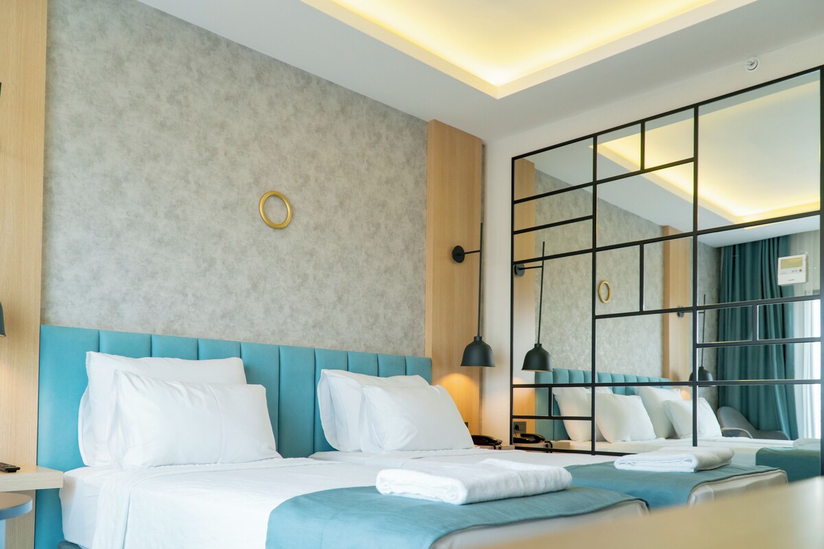 A modern hotel room with a large bed, a bedside table, a mirror, and a view of the city.