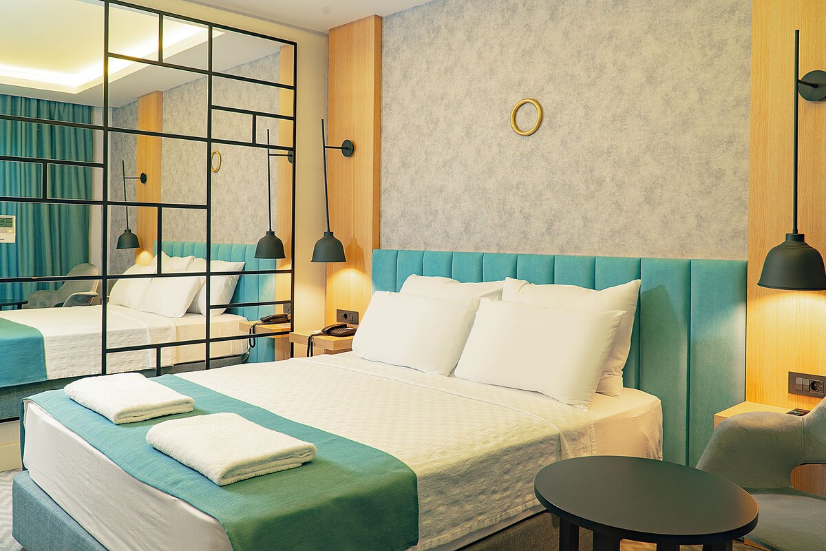 A hotel room with a large bed, a smaller bed, a round table, and a chair.