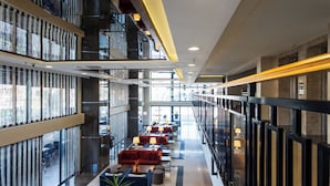 Um hall de hotel moderno com área de estar central, guarda-corpos de vidro e uma escadaria.