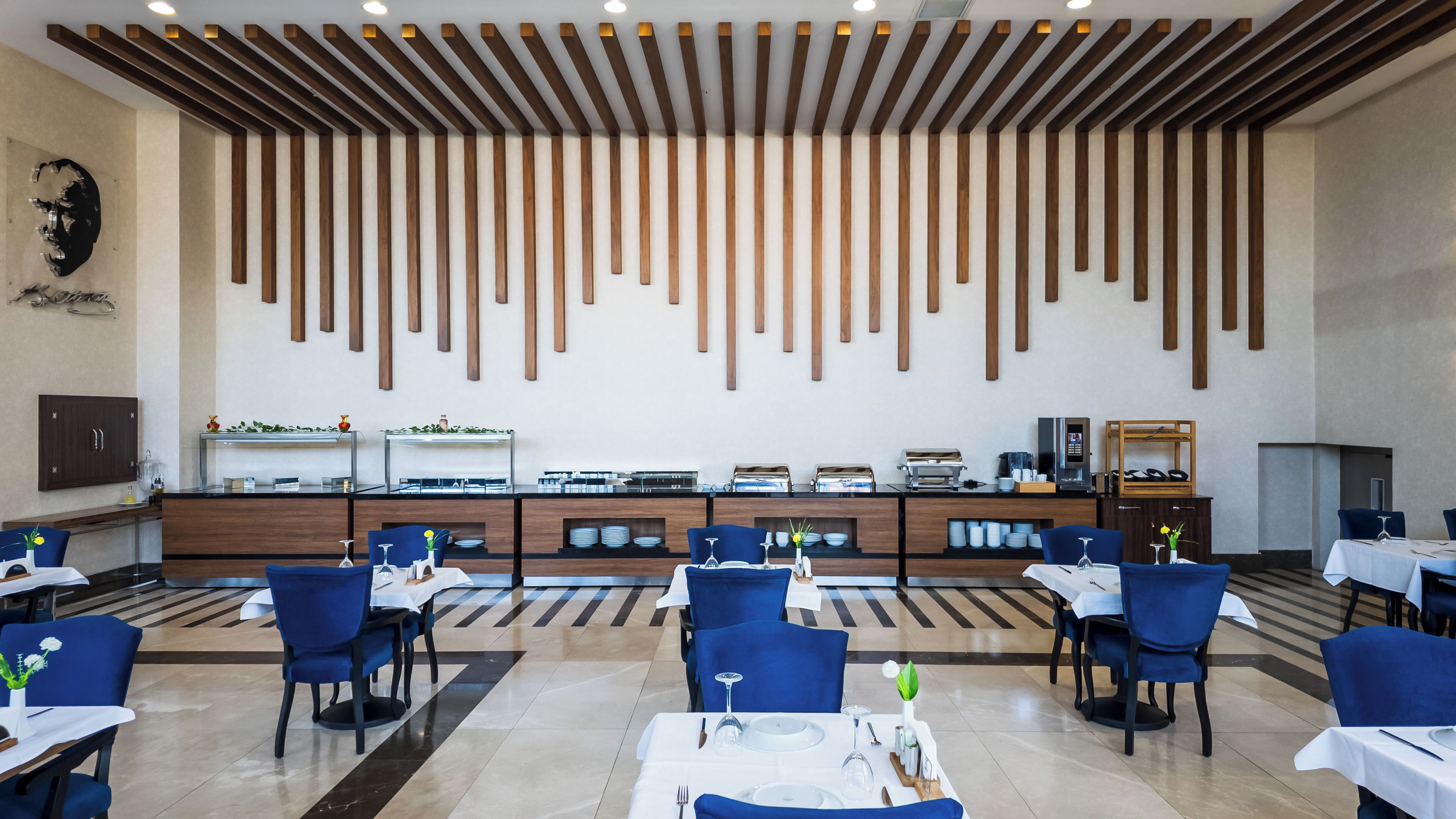 A modern dining area with a long counter, blue chairs, and a wooden ceiling design.