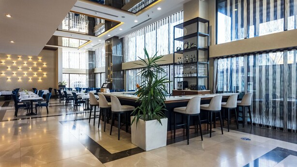 Um hall de hotel moderno com um bar central, áreas de estar e uma grande planta em vaso.