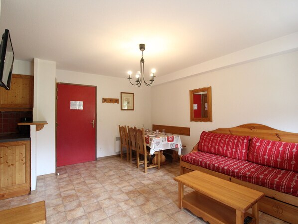Ein Wohnzimmer mit rotem Sofa, Holzmöbeln, einem Esstisch mit Stühlen und einer Küchenzeile mit Holzausbau.