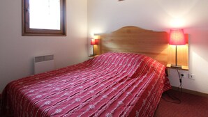 Une chambre à coucher avec une tête de lit en bois, une fenêtre avec des stores, une lampe de chevet et un tableau encadré accroché au mur.