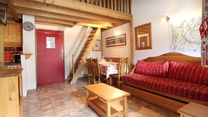 Une pièce chaleureuse avec un escalier en bois, une porte rouge, un canapé en bois et une table à manger avec des chaises.
