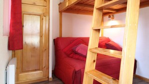 Una cama litera con escalera, un sofá rojo y un armario de madera en una habitación.