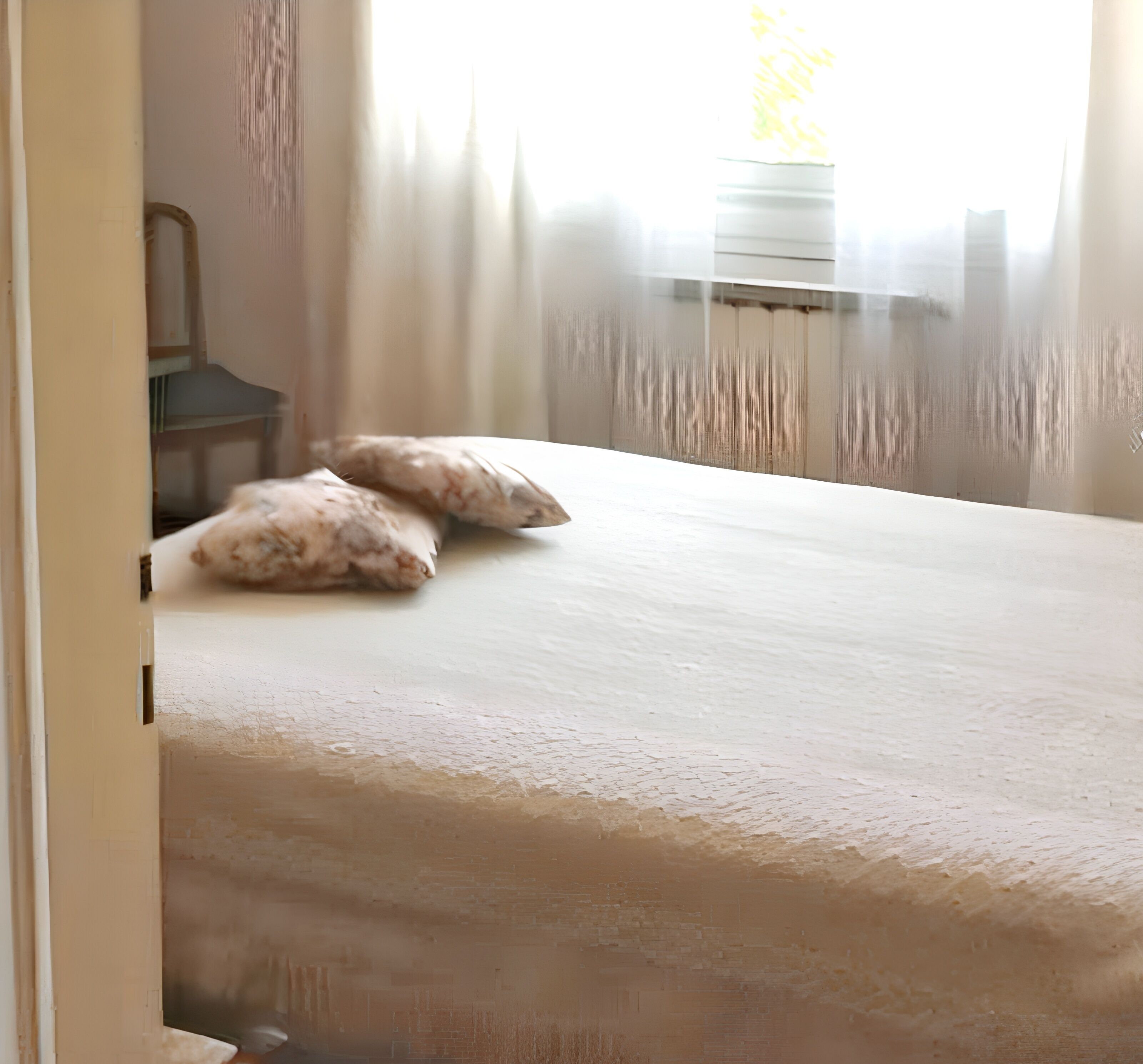 Quarto com cama, almofadas e janela com cortinas.