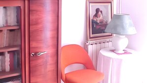 Une pièce avec une armoire en bois, une chaise orange et une table avec une lampe.
