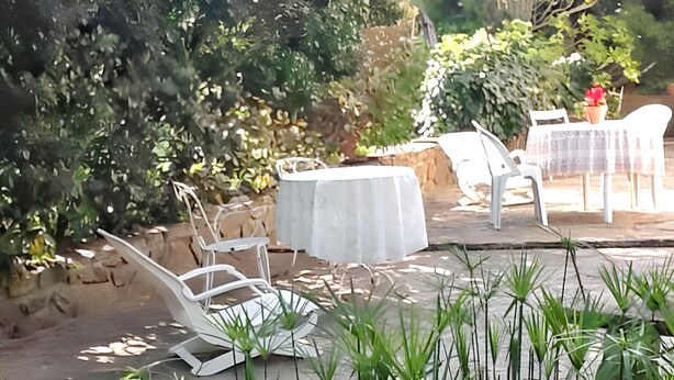 Une terrasse avec une table ronde et des chaises, entourée de verdure et d’un mur en pierre.