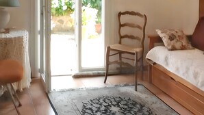 Une chambre à coucher avec un lit en bois, une chaise, une table et une vue sur l’extérieur grâce à une porte vitrée.