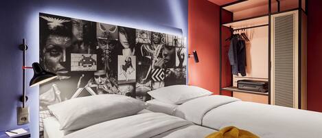 Un dormitorio moderno con una cama grande, un cabecero con un collage de imágenes, un armario con ropa colgada y una mesita de noche con una lámpara.