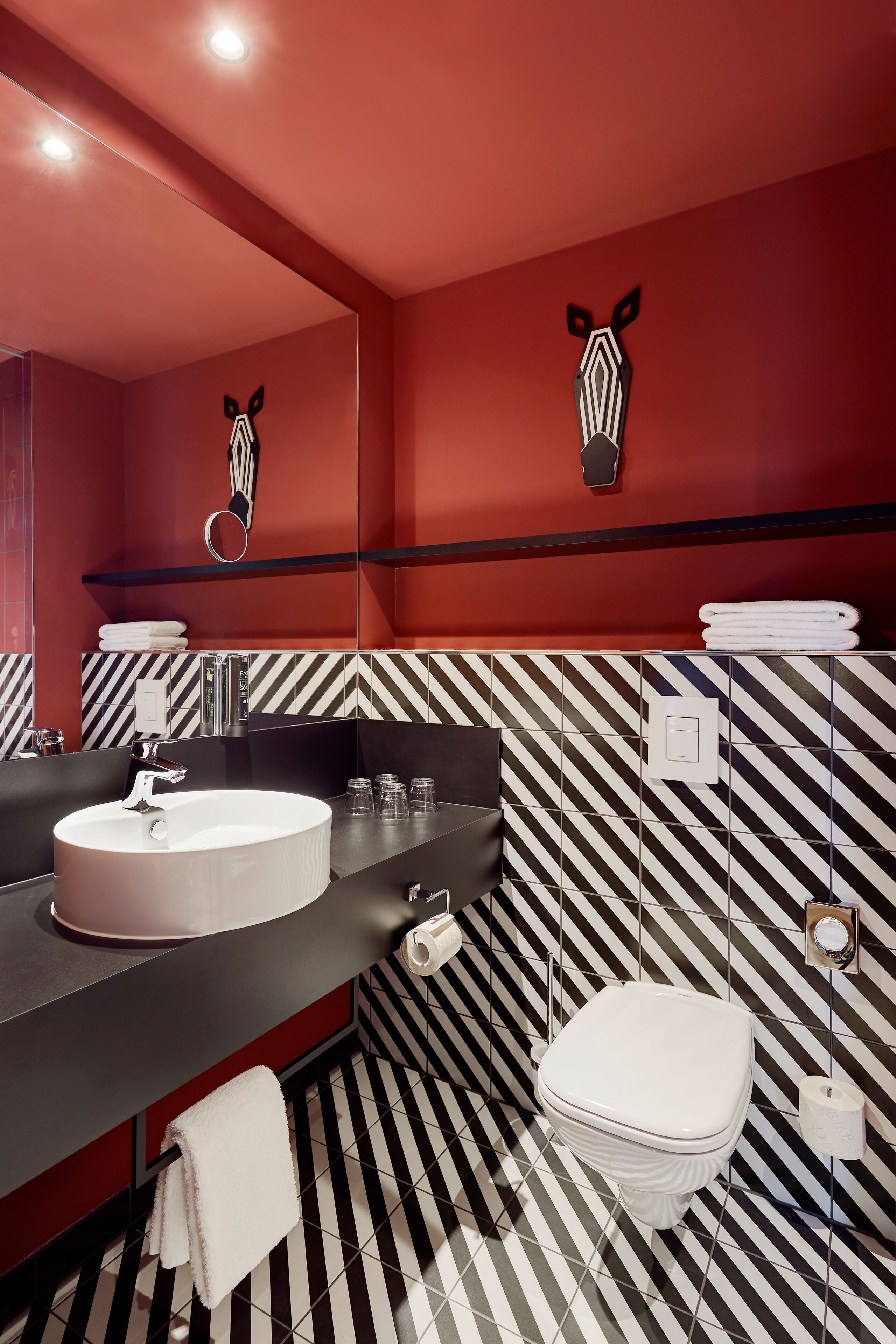 Un baño moderno con un lavabo redondo, un espejo, un adorno de cebra en la pared, un inodoro y un suelo a rayas.