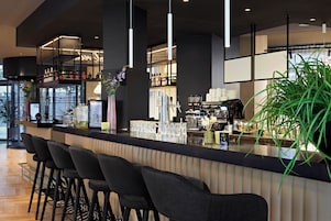 Un área de bar moderna con taburetes altos, una barra con utensilios para coctelería y una planta grande en maceta.