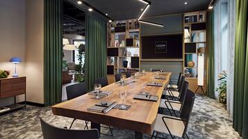 Un salón de conferencias con una larga mesa de madera, sillas y una estantería con diversos objetos.