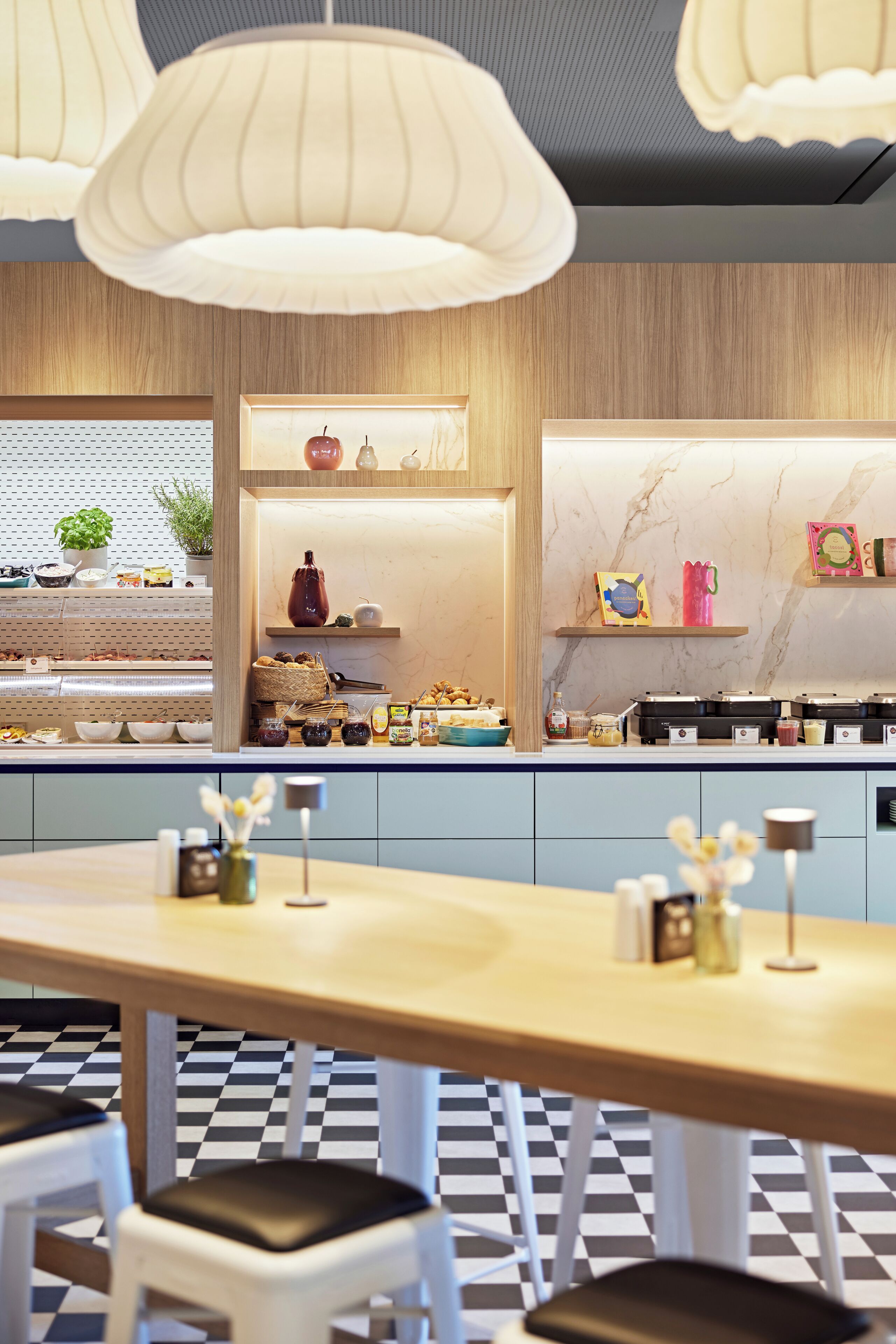 A restaurant with a checkered floor, wooden counter, and hanging pendant lights.