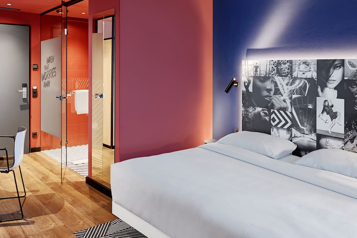 A modern hotel room with a bed, a glass shower enclosure, a seating area, and a wall with black and white photographs.