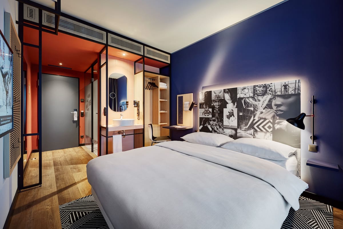 A modern hotel room with a large bed, a desk, and a walk-in closet.