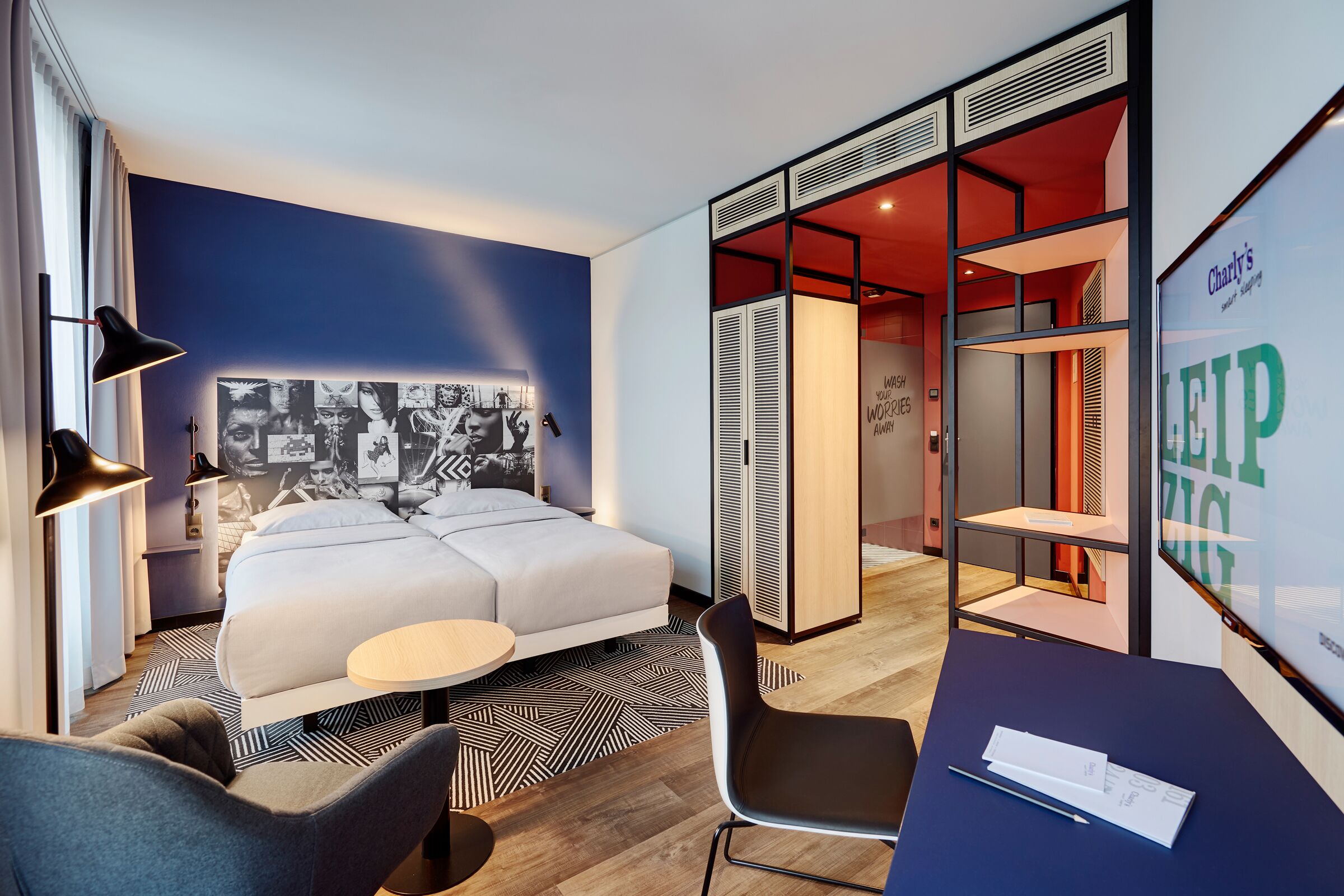 Una habitación de hotel moderna con una cama grande, un escritorio con una silla, una lámpara de pared y un cartel.