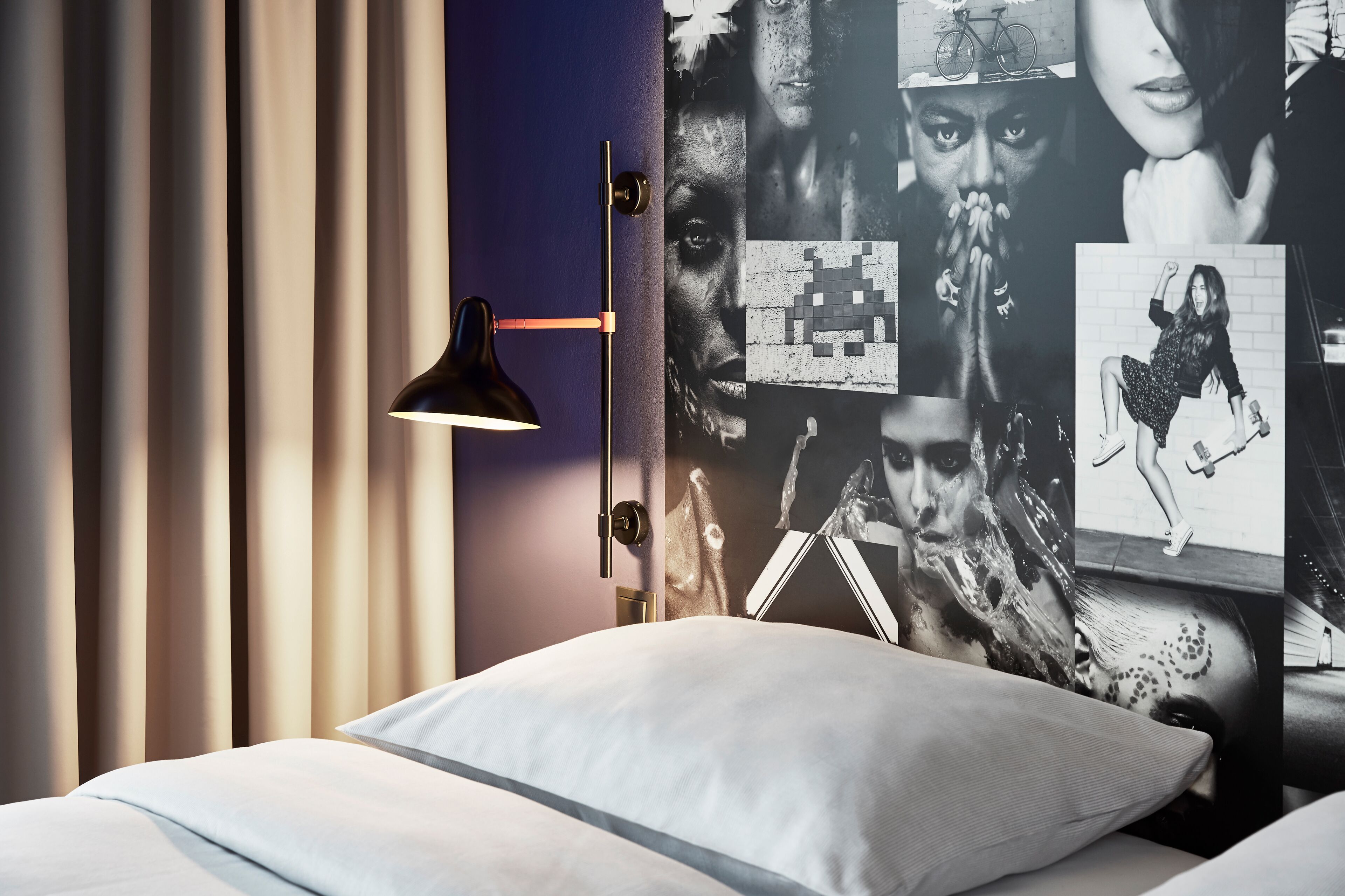 Een slaapkamer met een bed, nachtkastje, lamp en een muur met verschillende posters.