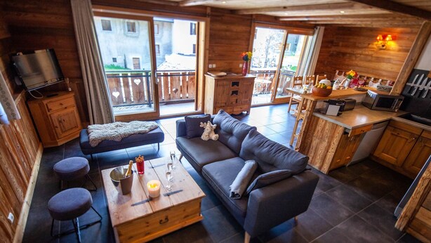 Une pièce confortable, aménagée comme un chalet, avec un canapé, une table basse, un téléviseur et un coin cuisine doté de meubles en bois et d’une table à manger.