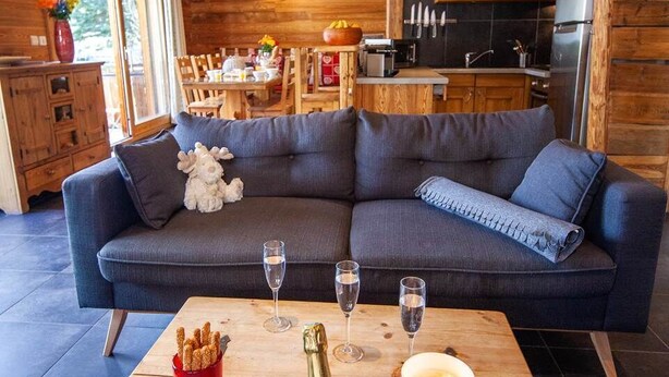 En hyggelig stue med en mørkeblå sofa, et træbord med champagne, glas og et lys.