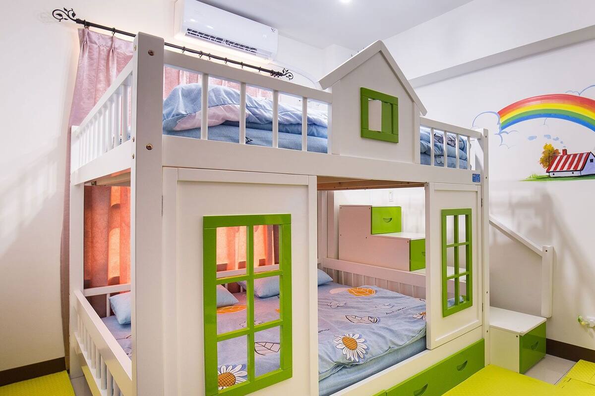 A bunk bed with a house design, featuring a window, a door, and a small table.