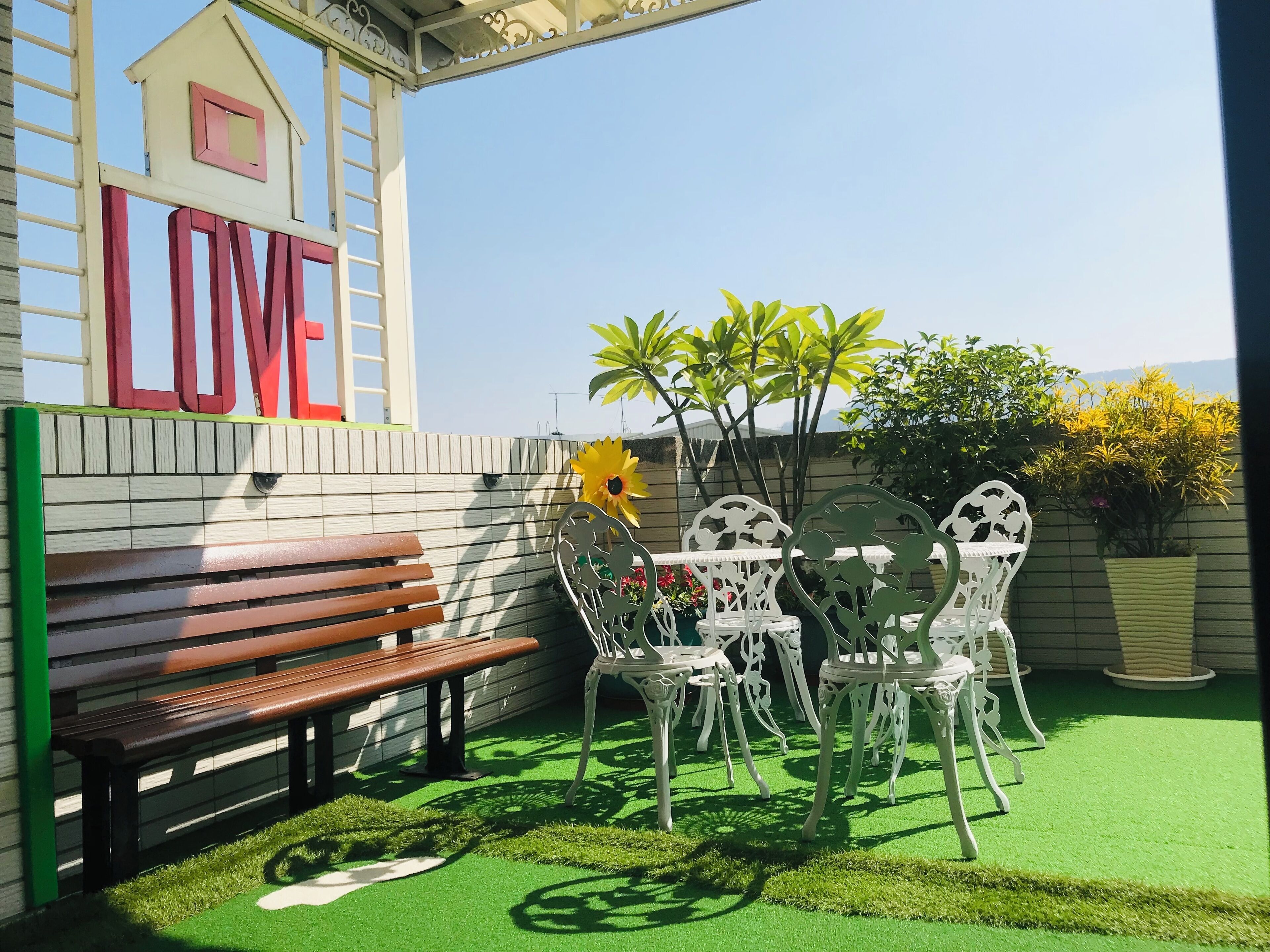 A patio area with a wooden bench, white metal chairs, and a table. A large 'LOVE' sign is visible on the wall.