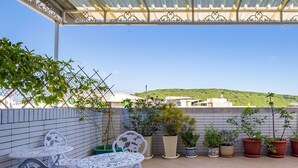 A covered patio with white metal chairs and tables, surrounded by potted plants and a view of a hill. - J.S 23 Kids Homestay (Kaohsiung)