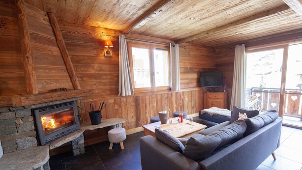 Une pièce chaleureuse avec une cheminée en pierre, un canapé, une table avec des boissons et un téléviseur fixé au mur.